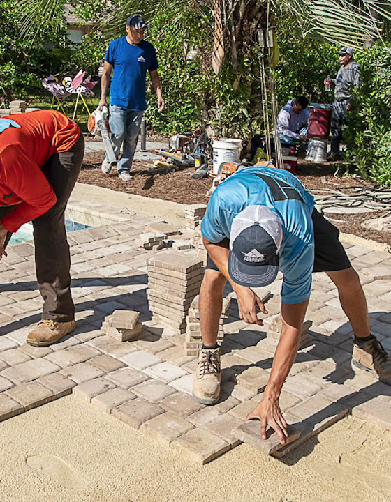 This image shows men placing pavers on a pool deck.